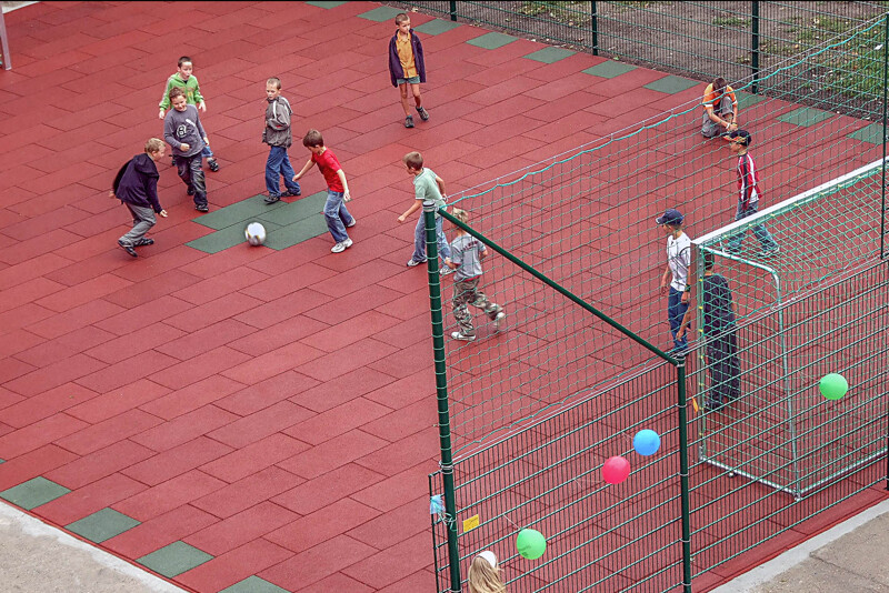 Les enfants jouent au foot sur un nouveau terrain de foot fait de dalles en caoutchouc rouges et vertes de WARCO. 