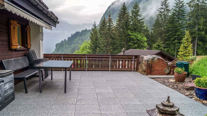 Sur fond d Alpes suisses, il y a un chalet avec une terrasse spacieuse couverte de dalles de terrasse WARCO en couleur granit clair.