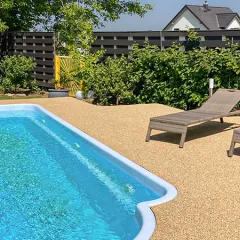 Privater Pool mit beiger Umrandung, Liegestühlen und üppiger Bepflanzung: Die WARCO Poolumrandung ist rutschhemmend, angenehm barfuß begehbar, hitzebeständig und pflegeleicht – ideal für sicheres Baden und entspanntes Sonnen.