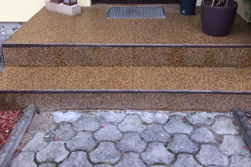 Un entrée d'une maison a été partiellement rénovée. Un escalier est recouvert de sol WARCO en Terre cuite. Le chemin qui mène à la maison reste en pavé de béton.