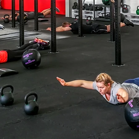 Des personnes allongées sur le sol élastique font de l'exercice dans un gymnase. Le sol est constitué de tapis sportifs de portection WARCO.
