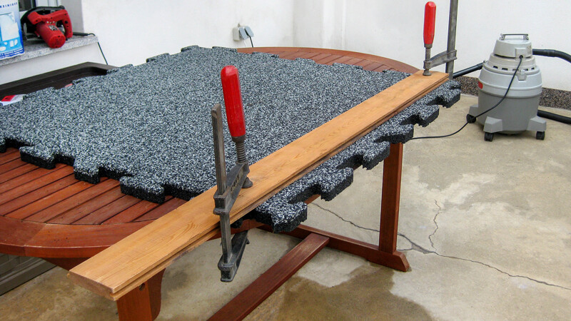 Fixée sur une table de jardin à l aide de deux serre-joints à vis, la dalle en caoutchouc est préparée pour la découpe précise