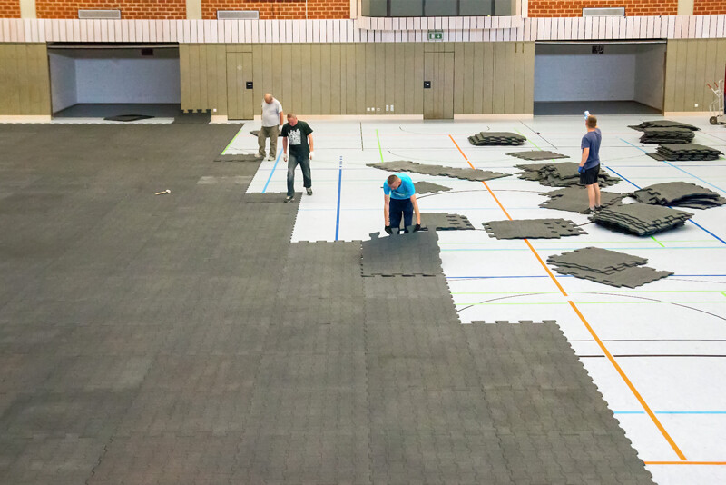Les tapis amortissants pour protection de sol WARCO sont posés dans un grande gymnase par 4 utilisateurs.