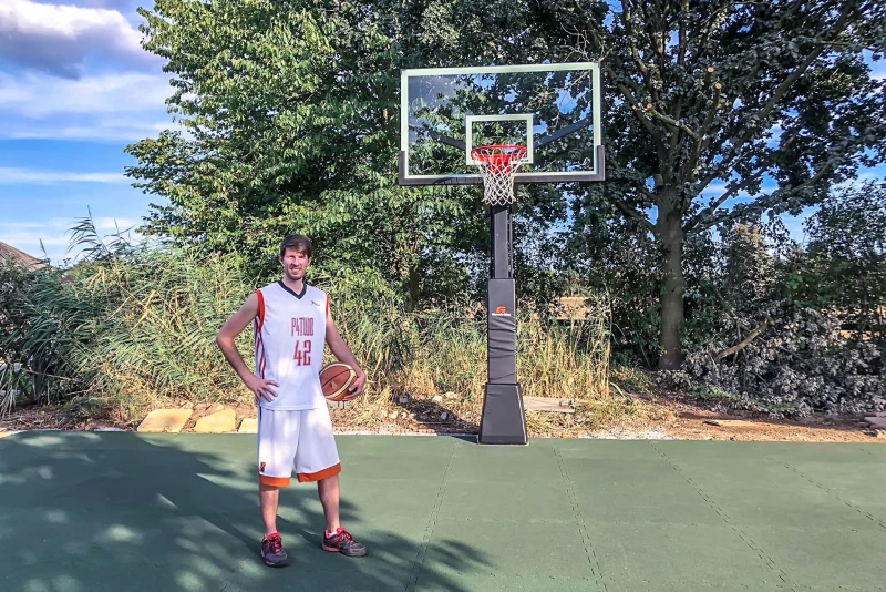 Sur un terrain de basket dans le jardin avec des dalles de jeu de ballon WARCO en vert gazon, il y a un grand joueur de basket. Le bon rebond du ballon réponde aux exigences des joueurs de basket.