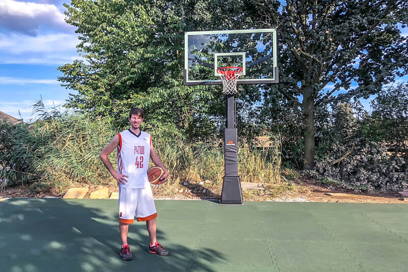 Sur un terrain de basket dans le jardin avec des dalles de jeu de ballon WARCO, il y a un grand joueur de basket.