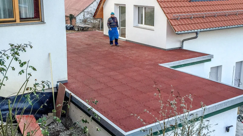 Entre deux maisons unifamiliales, il y a un garage avec un toit plat qui est conçu comme une terrasse constituée de dalles rouges de WARCO.