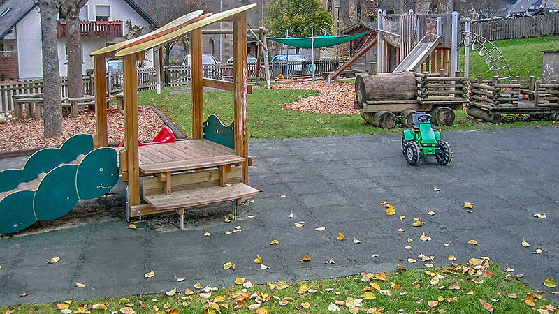 Un grand terrain de jeux naturel à Olsberg fait de dalles antichoc WARCO grises avec une petite maison de jeu en bois.
