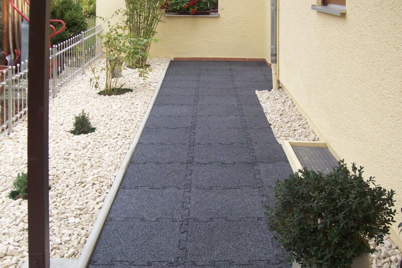 Une trottoir faite de dalles en caoutchouc noir mène par le jardin moderne et élégant en gravier vers la porte entrée.